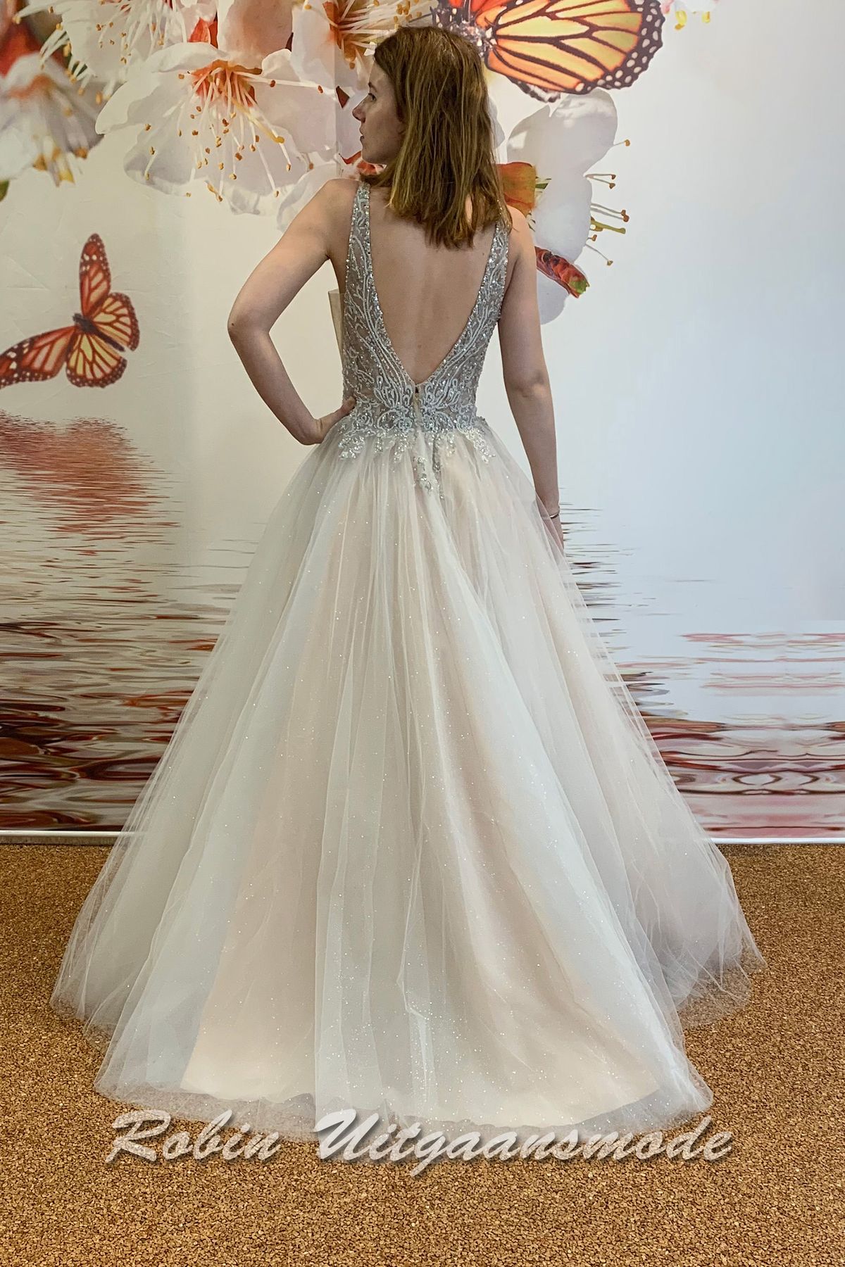 Achterkant van de Ivoorkleurige glamour trouwjurk met kralen versierd lijfje, een illusie diep V-hals, brede schouderbanden, blote schouders en A-lijn glittertule rok