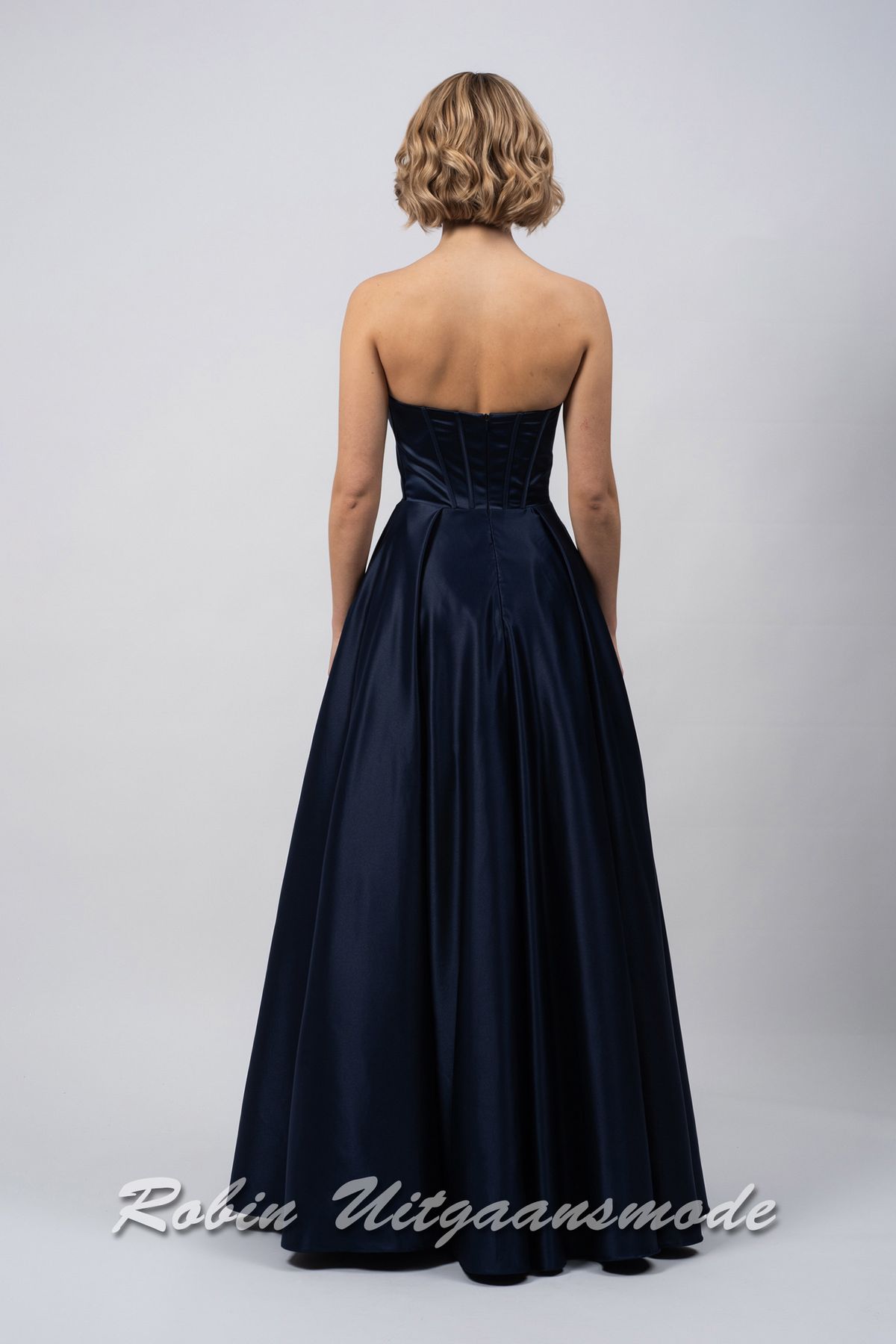 Achterkant van de Strapless inktblauwe avondjurk met A-lijn rok, een heartshape bustelijn versierd met sprankelende pailletten en afgewerkt met waterval band